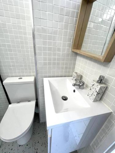 a white bathroom with a toilet and a sink at Charming beachfront Strand apartment in Cape Town