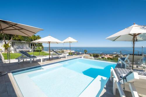 a swimming pool with umbrellas and the ocean at Clifton Sunset, Does have Power! in Cape Town