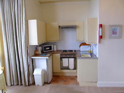 a small kitchen with white cabinets and a refrigerator at Redsands Villa in Torquay