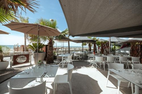 a restaurant with white tables and umbrellas and the ocean at Appartement 1ere ligne piscine terrasse au bord de la plage front de mer avec 6 vélos in Palavas-les-Flots