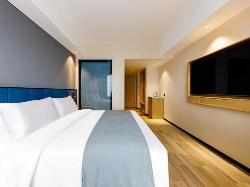 a large white bed in a hotel room with a flat screen tv at LanOu Hotel Xuchang Caowei Ancient City in Xuchang
