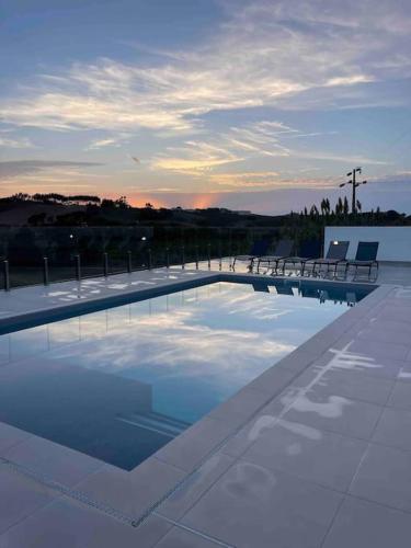 a swimming pool with benches and a sunset in the background at Casas de Campo - Vale da Terça in Vermelho