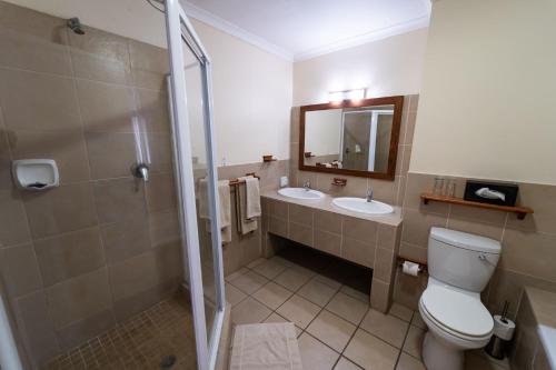 a bathroom with a toilet and two sinks and a shower at Gooderson Drakensberg Gardens Golf & Spa Resort in Drakensberg Garden