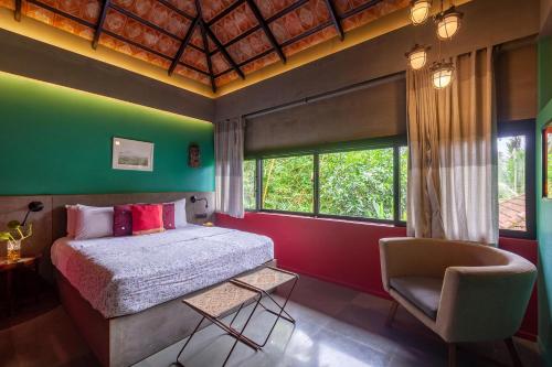 a bedroom with a bed and a chair and windows at StayVista at Toya Toya River View in Kozhikode