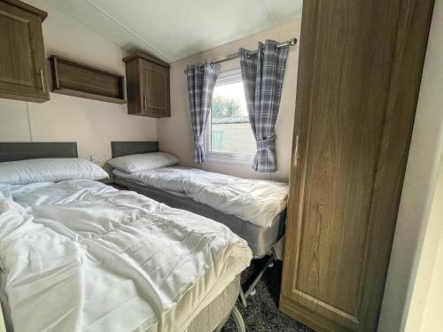 Duas camas num pequeno quarto com uma janela em Homely Dog Friendly Caravan At California Cliffs Holiday Park, Ref 50024j em Great Yarmouth