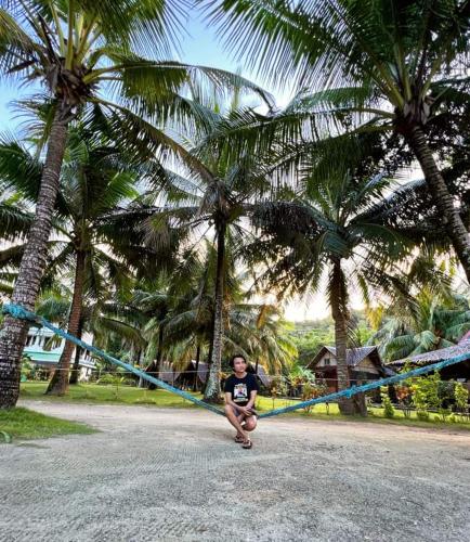 a man sitting on a blue rope between two palm trees at KOKONUT HUT RETREAT & CAMPING SITE RENTAL in Romblon
