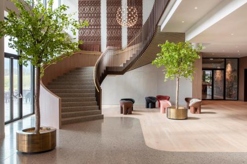 a lobby with a staircase and two trees and chairs at Van der Valk Hotel Deventer in Deventer