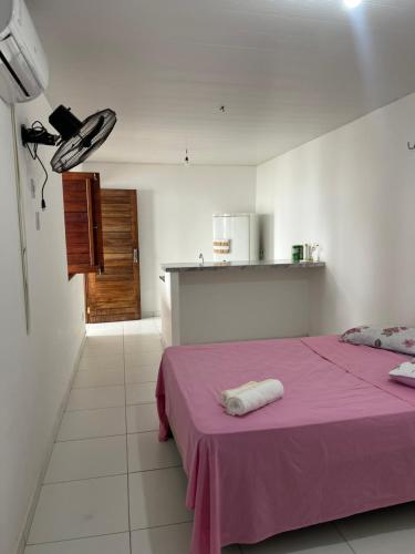 a room with a bed with a pink blanket and a kitchen at Reis Veloso in Parnaíba