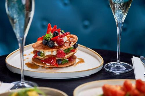 a plate of pancakes with fruit on a table with glasses at The Clermont London, Victoria in London
