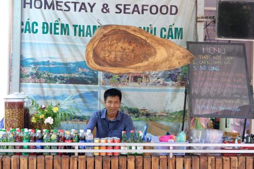 Un uomo in piedi dietro un bancone in un chiosco di cibo di Phú Sĩ Homestay và Seafood Núi Cấm 
