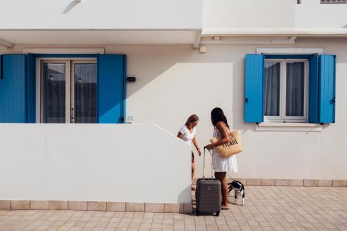 two women standing next to a wall with luggage at Anima Jesolo - Drago Village - Family Apartments - City Center, Pool & Garden, Beach Umbrella Included, 2 Parking Spaces in Lido di Jesolo