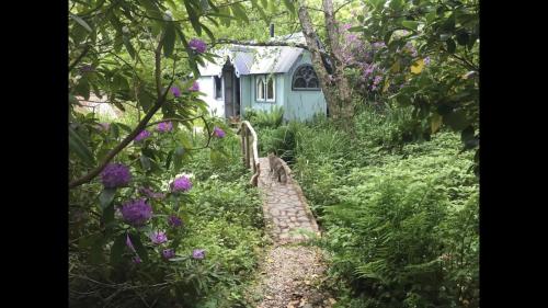 a garden with purple flowers in front of a blue house at Magical Tabernacle in a Beautiful Setting with Hot Tub in Bude