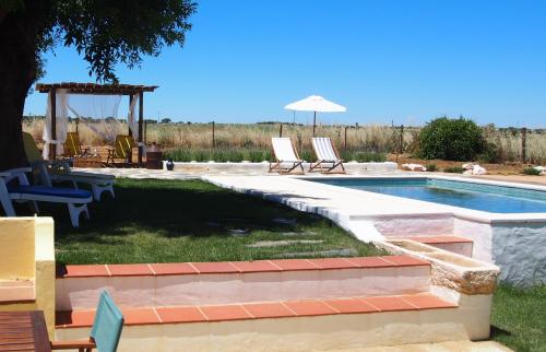 a swimming pool in a yard with chairs and an umbrella at Monte dos Freixos Country House in São Lourenço de Mamporcão