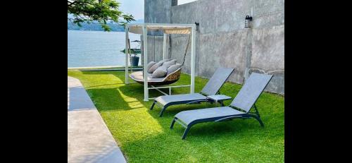 two chairs and a swing on the grass near the water at Casa del Castillo in Tequesquitengo