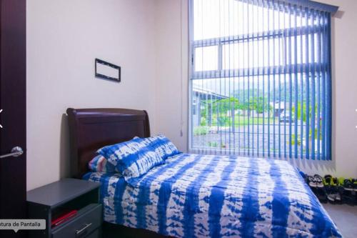 a bedroom with a bed with a blue blanket and a window at CASA DE PLAYA AMUEBLADA in Quebrada Ganado