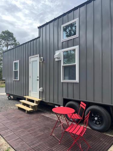 a black tiny house with two red chairs and a table at The Big Bend Tiny Home in Perry