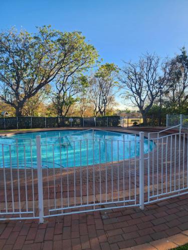 einen Zaun um einen Pool mit Bäumen im Hintergrund in der Unterkunft The lion Sands Apartment in Pretoria