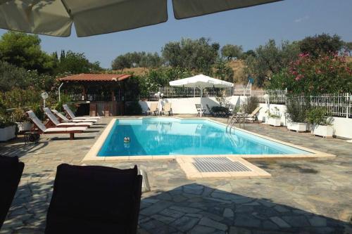a swimming pool in a yard with chairs and an umbrella at Villa Evridiki - Walking distance to beach in Porto Heli