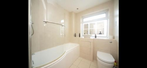 a bathroom with a tub and a toilet and a window at Spacious Chessington home with parking & garden in Chessington