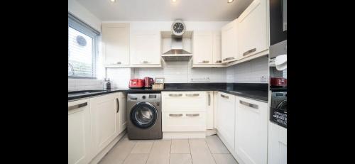a kitchen with white cabinets and a washing machine at Spacious Chessington home with parking & garden in Chessington