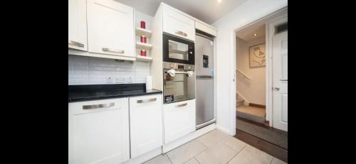 a white kitchen with white cabinets and a hallway at Spacious Chessington home with parking & garden in Chessington