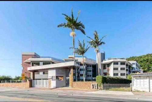 a building with two palm trees in front of it at Ape frente praia Ponta das Canas/3min Canasvieiras in Florianópolis