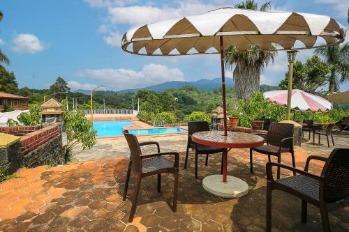 uma mesa e cadeiras com um guarda-sol ao lado de uma piscina em Hotel Pie de la Sierra em Uruapan del Progreso