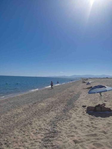 a beach with umbrellas and a person walking on the beach at Torreilles-Casa terracota-plage - visa image- les déferlantes le Barcares - South of France in Torreilles