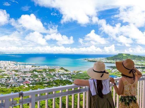 dos chicas de pie en un balcón con vistas al océano en The Yuinchi Hotel Nanjo en Nanjo