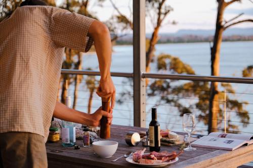 a man is preparing food on a table with wine bottles at Baragoola Retreat - Luxury Waterfront Property in Sandford