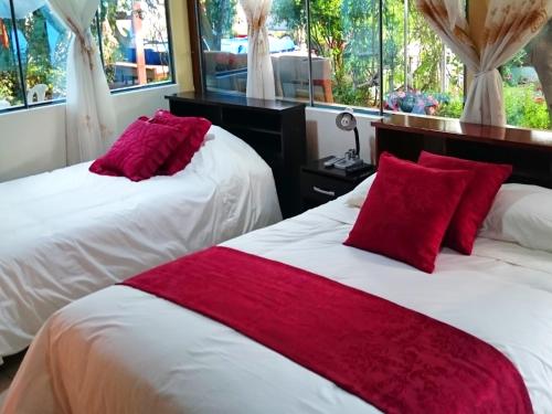 2 camas con almohadas rojas en una habitación con ventanas en Hostal el Parque Tababela, en Tababela