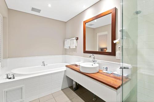 a bathroom with a sink and a tub and a mirror at Caves House Hotel Apartments in Yallingup
