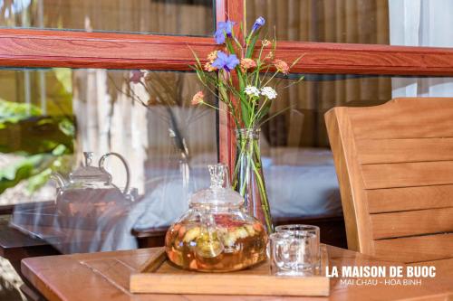 ein Glasgefäß mit einer Vase mit Blumen auf dem Tisch in der Unterkunft La Maison De Buoc in Mai Châu