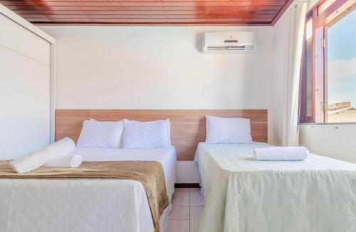 1 dormitorio con 2 camas con sábanas blancas y ventana en Guarajuba - casa em condomínio corais a 200 metros da praia, en Camaçari
