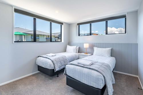 two beds in a room with two windows at Stylish Panoramic Mountain and Lake Views in Wanaka
