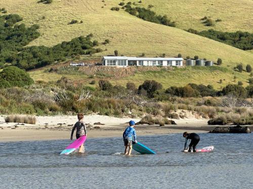 three boys are standing on surfboards in the water at Middle River Vista Beach House in Stokes Bay