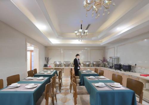 a man standing in a dining room with tables at Vienna International Hotel - Shanghai Jiaotong University Humin Road in Shanghai