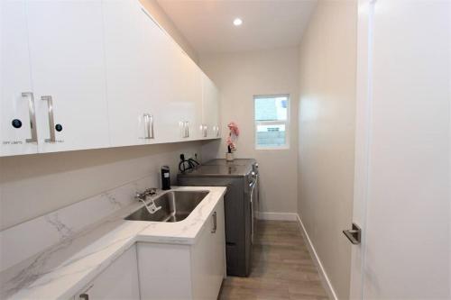 a white kitchen with a sink and a dishwasher at New & Modern with Accessibility-Family Friendly in San Bernardino