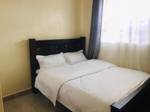 a bedroom with a bed with white sheets and a window at Citux Homes in Nairobi