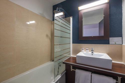 een badkamer met een wastafel, een bad en een spiegel bij The Originals City, Hotel Ariane, Toulouse in Toulouse