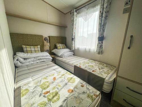 - 2 lits dans une petite chambre avec fenêtre dans l'établissement Spacious Caravan With Large Decking Area, Perfect To Enjoy The Sun, Ref 23058c, à Hunstanton