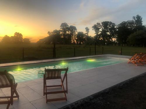 una piscina con 2 sillas y una puesta de sol en el fondo en Estancia Pedro Chico - Hotel Rural en Chascomús