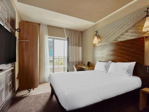a hotel room with a large white bed and a window at Ibis Aktobe in Aktobe