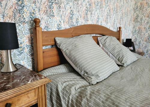 łóżko z drewnianym zagłówkiem oraz stół z lampką w obiekcie Gîte Moussette - Bord de Mer - 4/6 pers. w mieście Quinéville