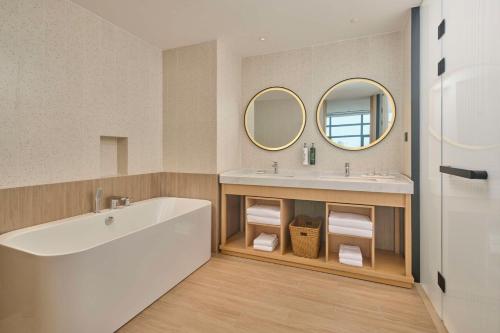 a bathroom with a tub and a sink and mirrors at Hilton Garden Inn Zhuhai Jinan University in Zhuhai