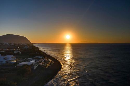 a sunset over a body of water with a town at Sea Breeze Santorini Beach Resort, Curio By Hilton in Perivolos