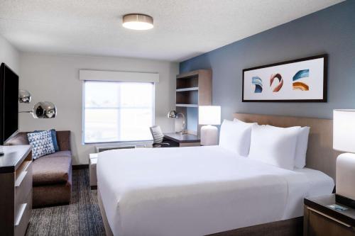 Hyatt House Colorado Springs Airport في كولورادو سبرينغز: غرفة نوم بسرير ابيض كبير وغرفة معيشة