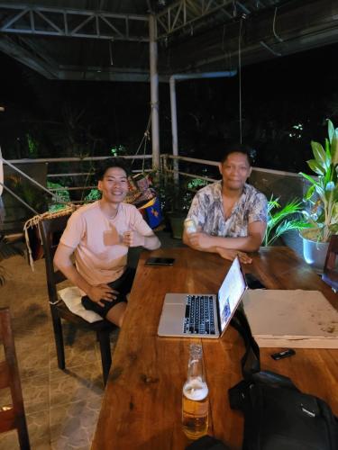 two men sitting at a table with a laptop at La Vida Hostel in Puerto Princesa City