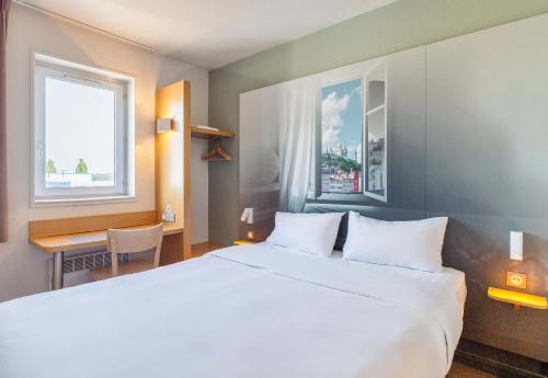1 dormitorio con 1 cama blanca grande y escritorio en B&B HOTEL Lyon Saint-Bonnet Mi-Plaine, en Saint-Bonnet-de-Mure