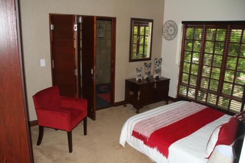 um quarto com uma cama e uma cadeira vermelha em White River Country Estate Self Catering Apartment em White River